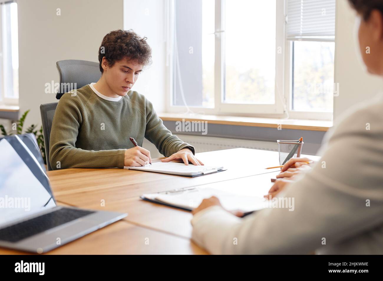 Porträt eines jungen Mannes, der im Vorstellungsgespräch mit dem HR-Manager einen Vertrag unterzeichnet, Platz kopieren Stockfoto