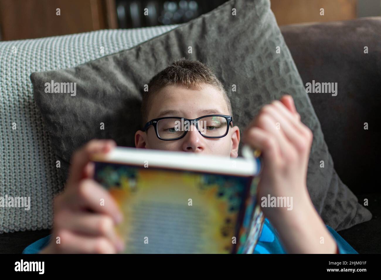 Kind mit Brille auf dem Sofa beim Lesen eines Buches Stockfoto