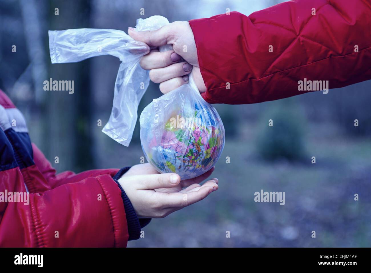 Hand eines kleinen Kindes, das sich ausstreckend einen Globus in Plastikbeutel von einem Erwachsenen nimmt, damit er sich um die Erde für seine Zukunft kümmern kann. Rette die Erde. Worl Stockfoto