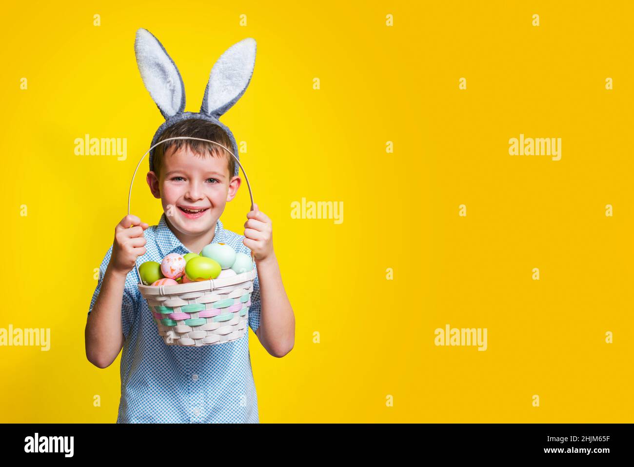 Süßes kleines Kind, das am Ostertag Hasenohren trägt und einen Korb mit bemalten Eiern hält. Glückliches Kind hält den Osterkorb in der Hand. Stockfoto