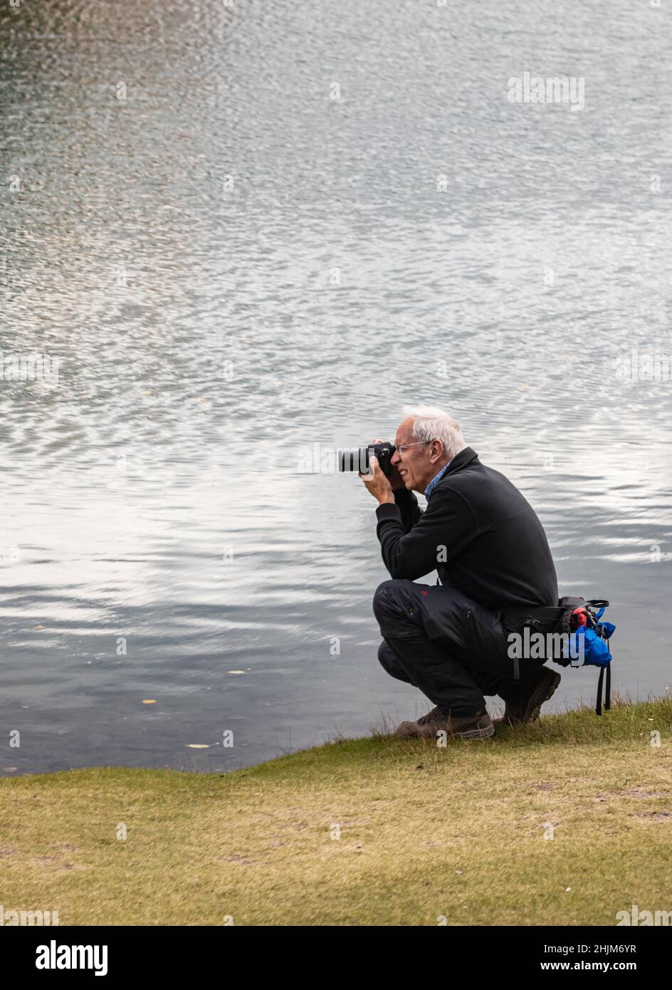 Älterer Rentner, der im Park fotografiert, Hobby im Freien. Aktive Langlebigkeit. Ein begeisterter und fröhlicher älterer Mann. Stockfoto