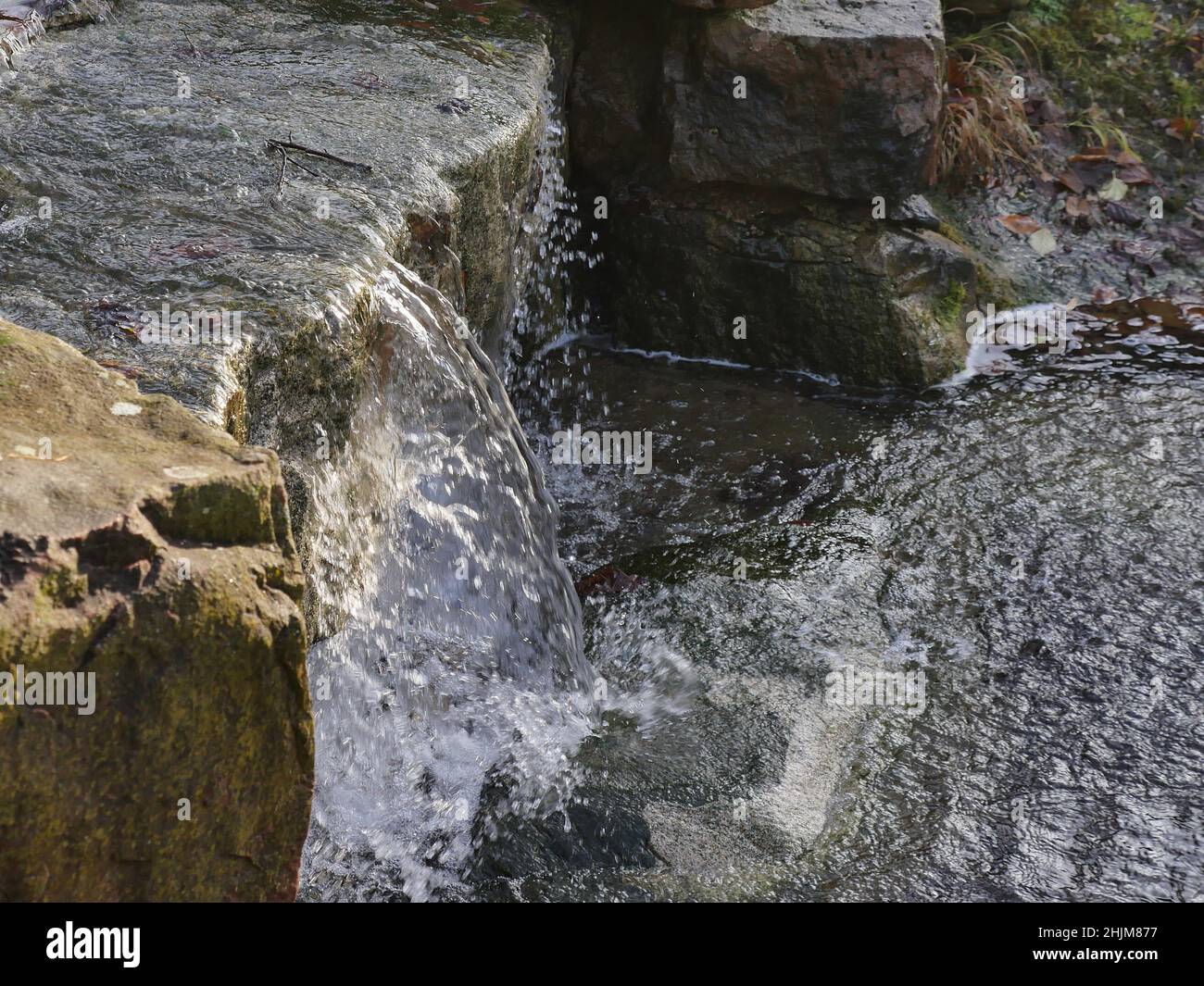 Bach zwischen zwei Felsbrocken, ein Miniatur-Wasserfall. Das Wasser spritzt auf felsigen Boden, wenn es auf den Boden trifft. Stockfoto