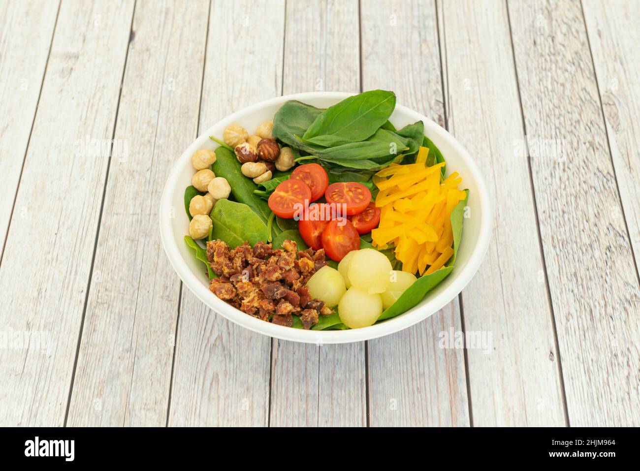 Spinatsalat, Kirschtomaten, geriebener gelber Pfeffer, gewürfelter Schinken, Melonenbällchen und geschälte Haselnüsse Stockfoto
