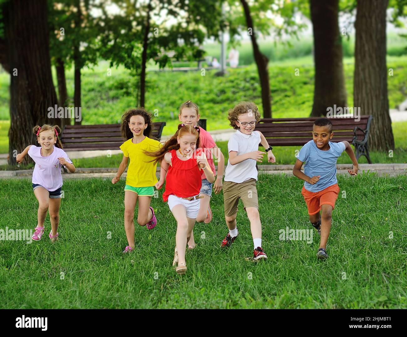 Eine Gruppe von Kindern von Jungen und Mädchen verschiedener Rassen laufen auf dem grünen Gras vor dem Hintergrund eines Erholungsparks. Kindertag, Stockfoto