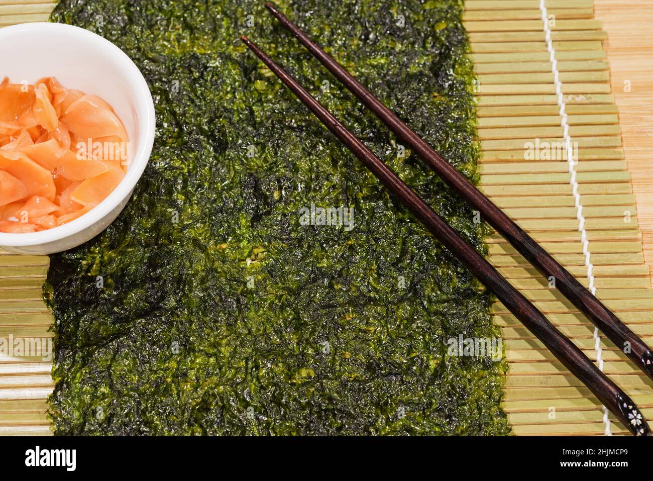 nori und eingelegter Ingwer und Essstäbchen auf einer Bambusmatte, bereit zum Sushi-Rollen Stockfoto