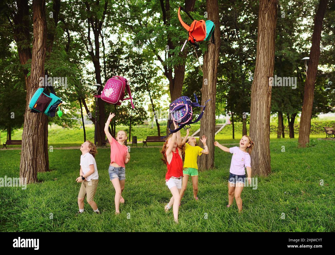 Eine Gruppe von Schulkindern freut sich zu Beginn der Sommerferien, schmeißt ihre Schulrucksäcke und lacht. Stockfoto