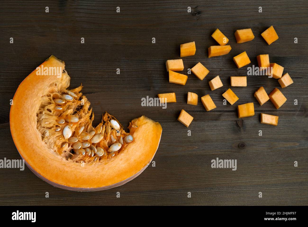 Frischer Bio-Kürbis in Scheiben geschnitten und auf einem dunklen Holztisch gewürfelt Stockfoto