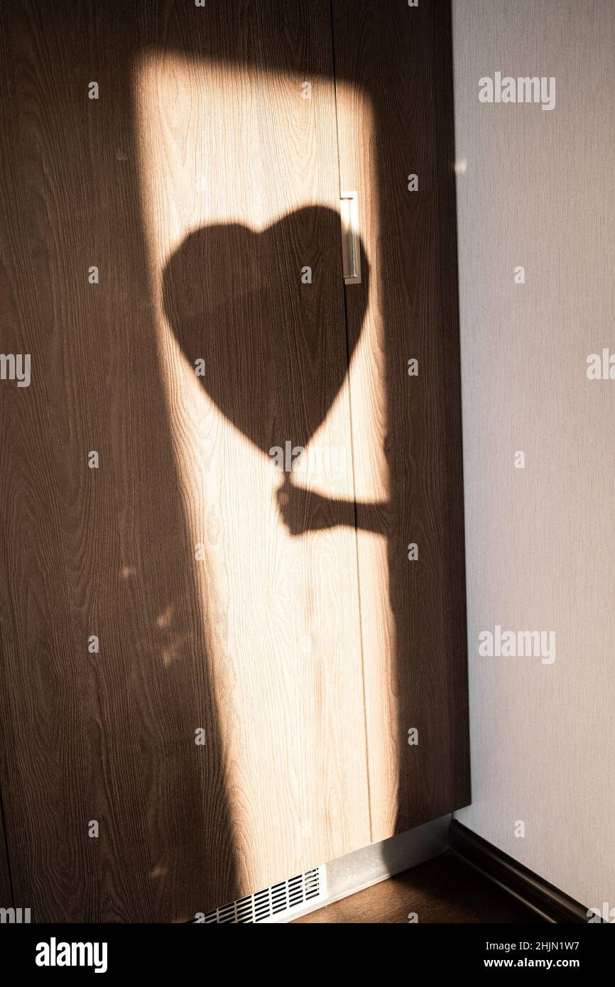 Romantik und Einsamkeit im Stadtschatten der Hand eines Mannes, der einen herzförmigen Ballon hält. Silhouette an der Wand. Suche nach Liebe Konzept, Stockfoto