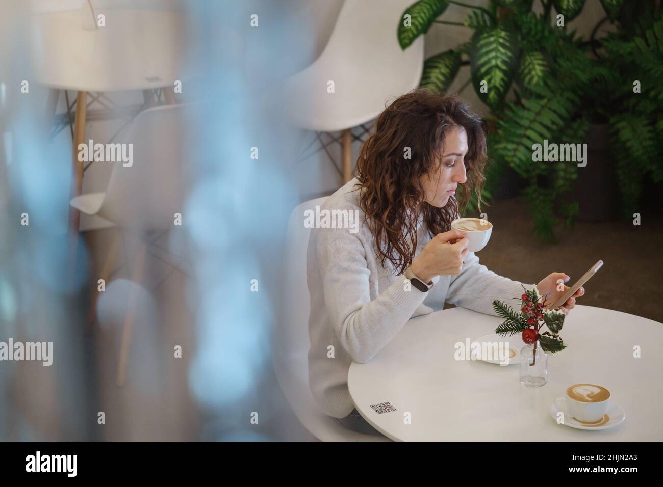 Frau trinkt im Winter Kaffee im Café. Verträumt entspannt erwachsenen Weibchen in ihrem 40s. Blick durch das Lametta. Reflexionen und Blendung Stockfoto