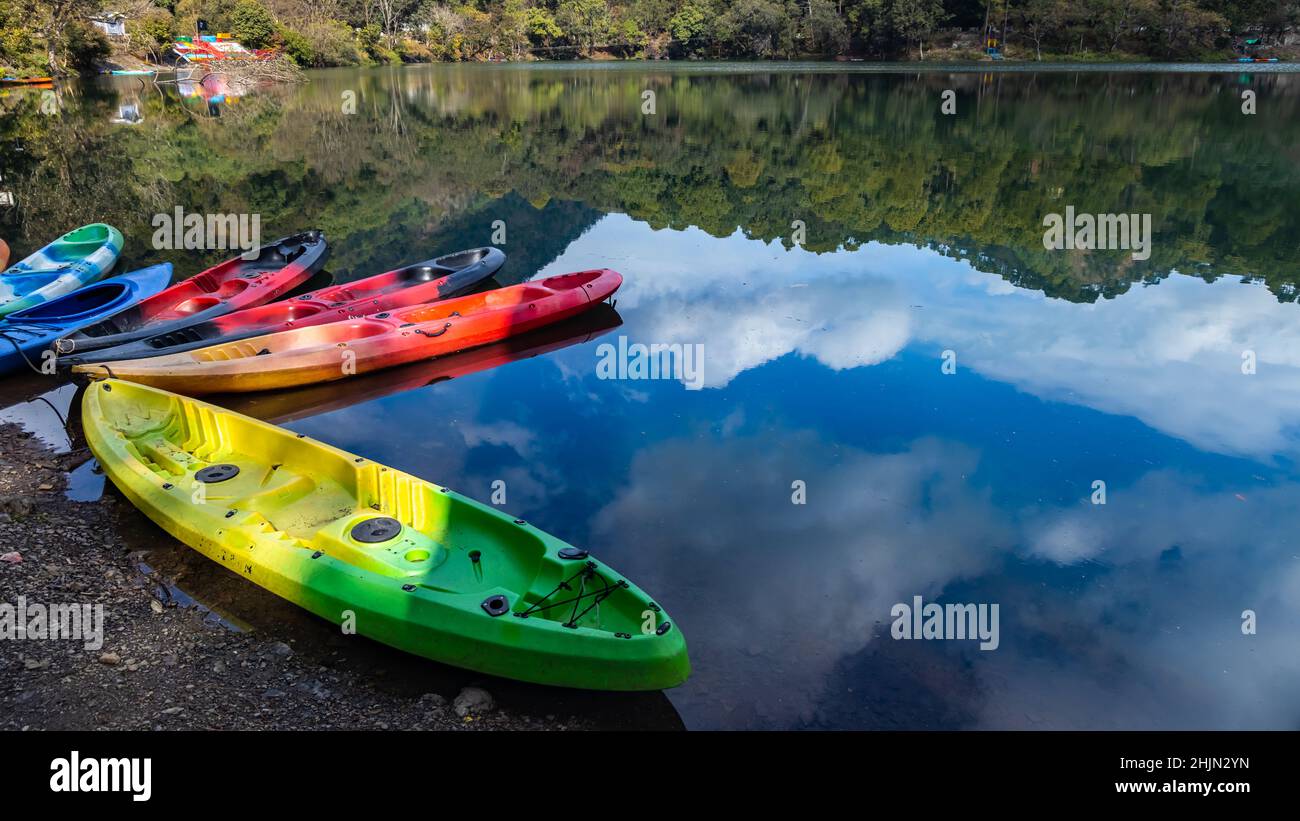 Bunte Boote am Ufer eines Sees mit der Spiegelung von Himmel und Hügeln Stockfoto