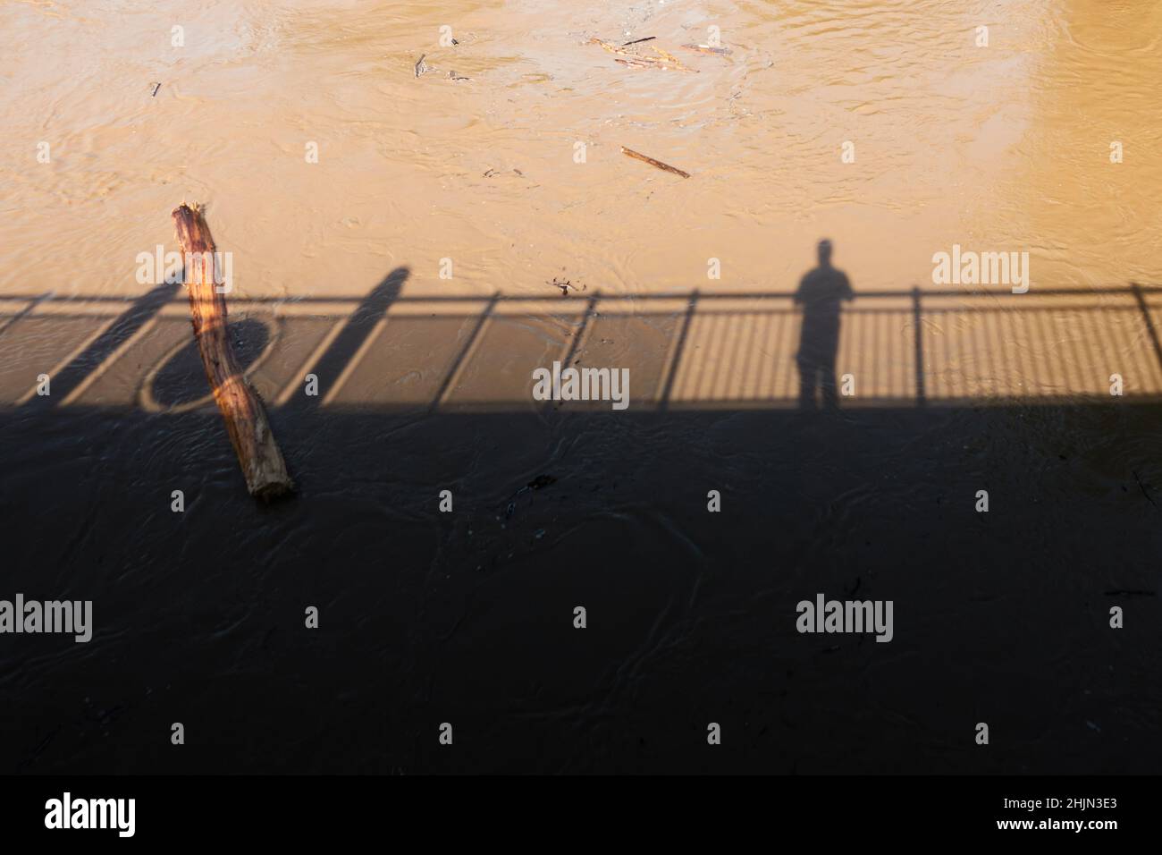 Silhouette eines Mannes, der auf einer Brücke steht. Driftwood wird von braunen Wassermassen weggespült. Hochwasser in Deutschland. High-Angle-Ansicht. Stockfoto