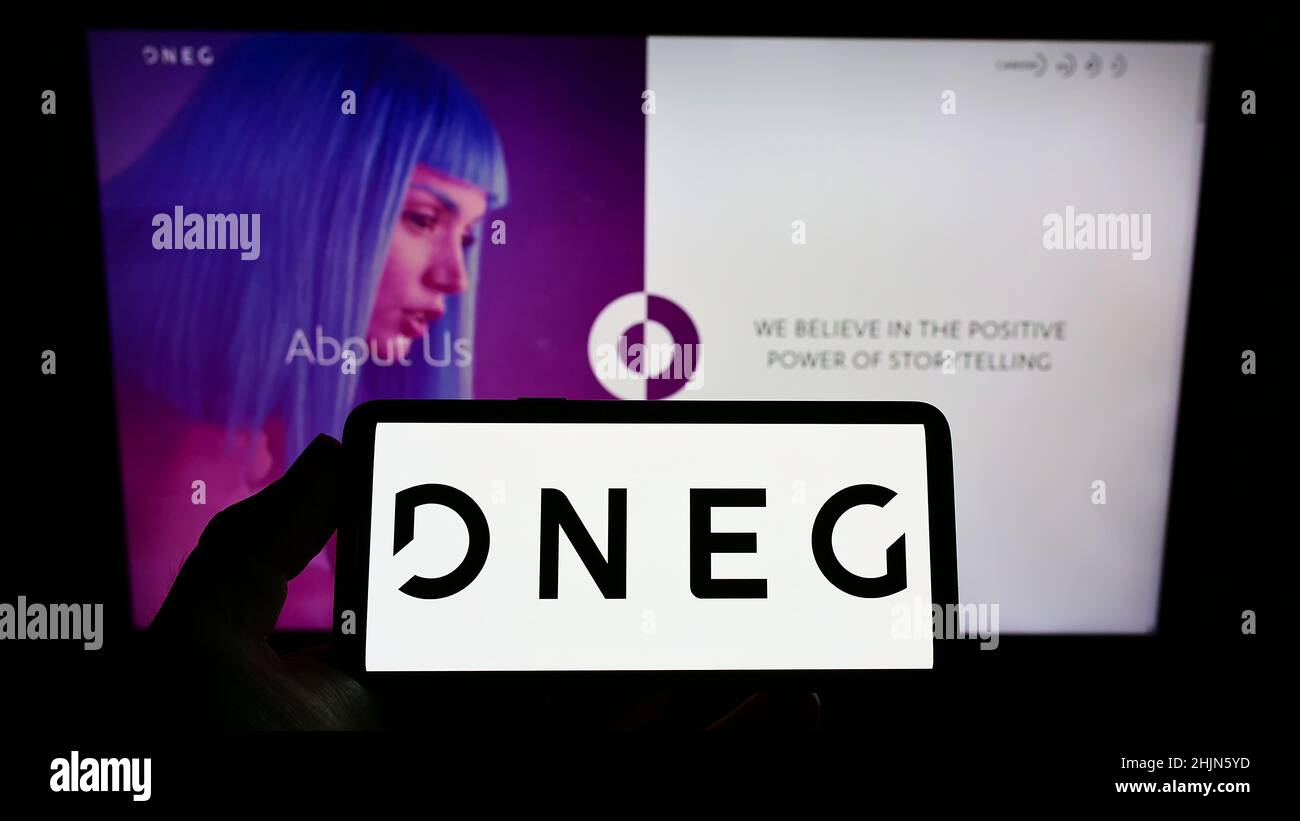 Person, die ein Smartphone mit dem Logo des britischen Unternehmens DNEG plc auf dem Bildschirm vor der Website hält. Konzentrieren Sie sich auf die Telefonanzeige. Stockfoto