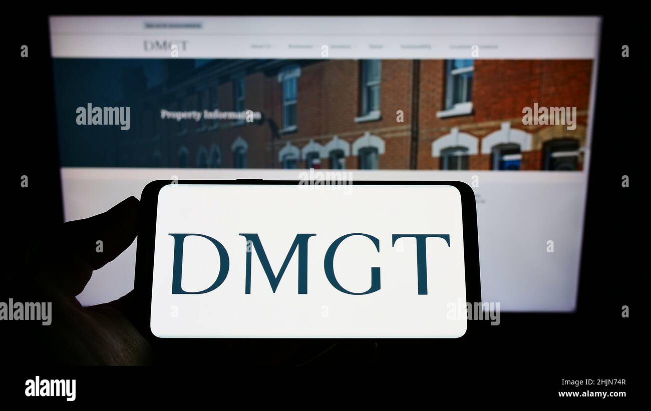 Person mit Mobiltelefon und Logo der Firma Daily Mail und General Trust plc (DMGT) auf dem Bildschirm vor der Webseite. Konzentrieren Sie sich auf die Telefonanzeige. Stockfoto