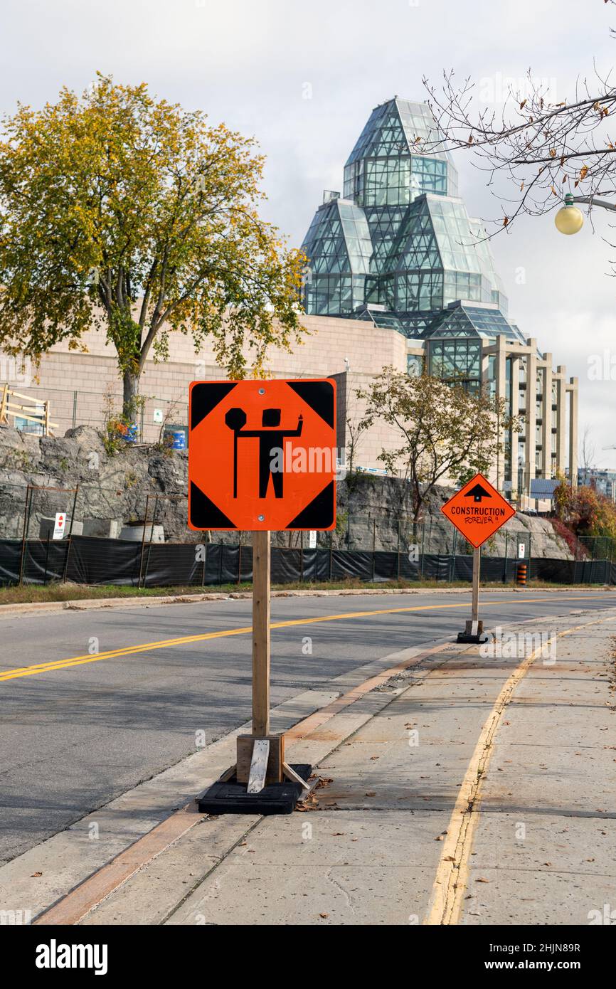 Ottawa, Kanada - 14. Oktober 2021: Verkehrskontrollperson vor dem Schild wegen Bauarbeiten in der Innenstadt der Stadt. Orangefarbenes Warnschild in der Nähe von t Stockfoto