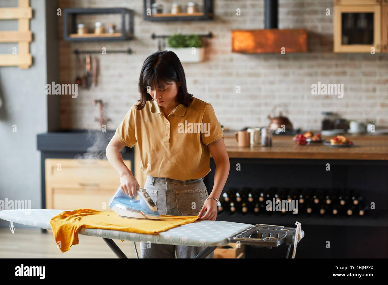Waist-up-Porträt einer jungen asiatischen Frau, die zu Hause Kleidung bügeln und Hausarbeiten erledigen, Platz kopieren Stockfoto