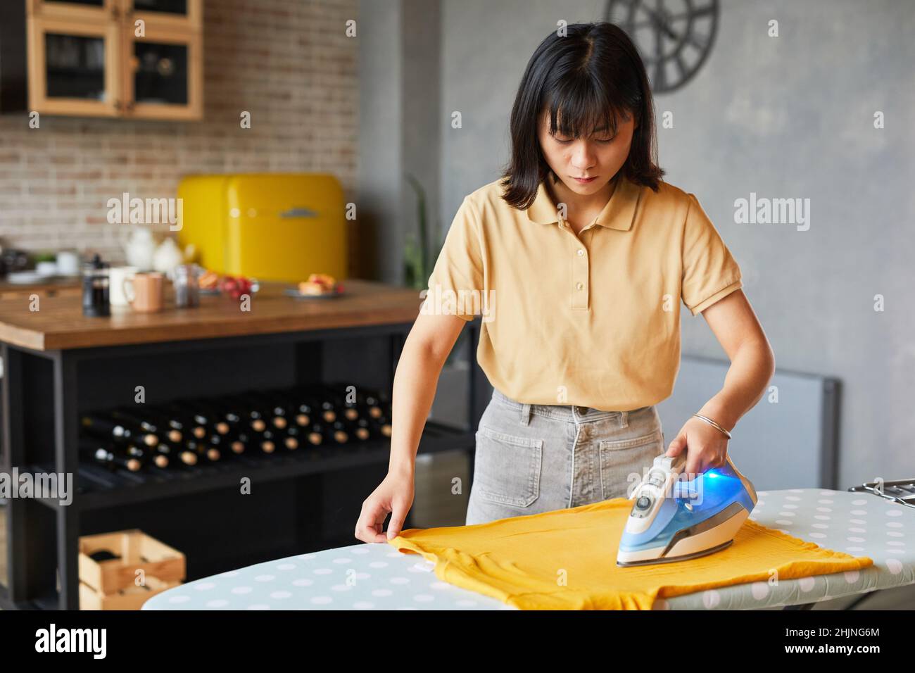 Waist-up-Porträt einer jungen Frau, die zu Hause Kleidung bügeln und Hausarbeiten erledigen, Platz kopieren Stockfoto