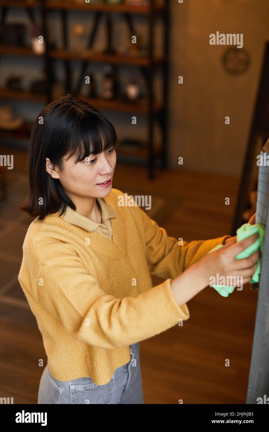Vertikale Seitenansicht Porträt einer jungen asiatischen Frau, die zu Hause putzt und staubt Stockfoto