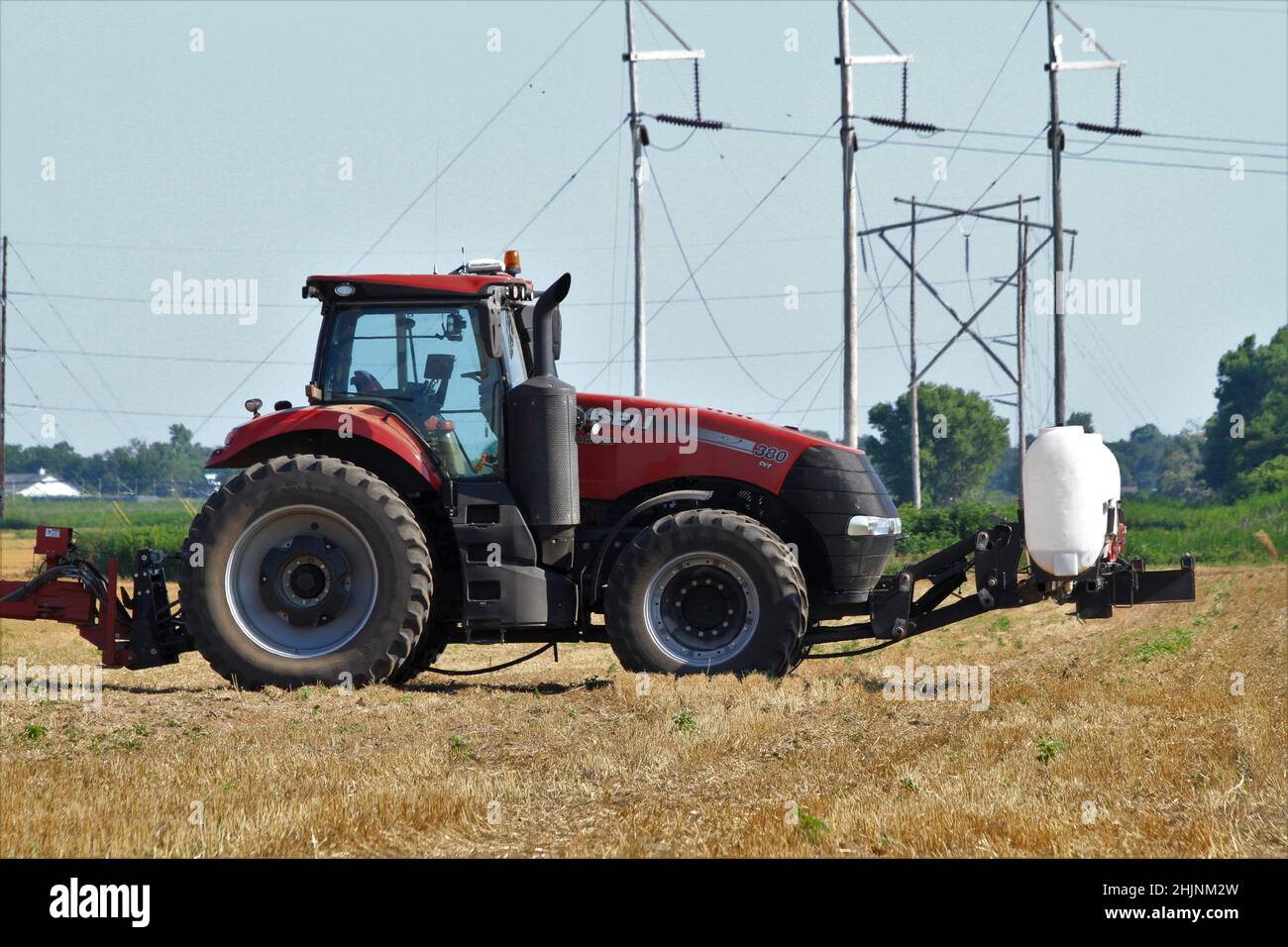 Ein Case International Traktor auf einem Feld mit Sprühgeräten auf der Rückseite mit blauem Himmel in Kansas im Land. Stockfoto