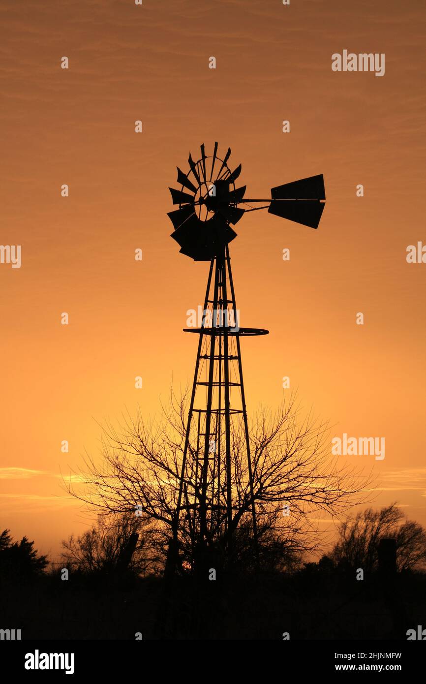 Ein farbenfroher Sonnenuntergang in Kansas mit goldenem Himmel und Windmühle auf einer Weide auf dem Land Stockfoto
