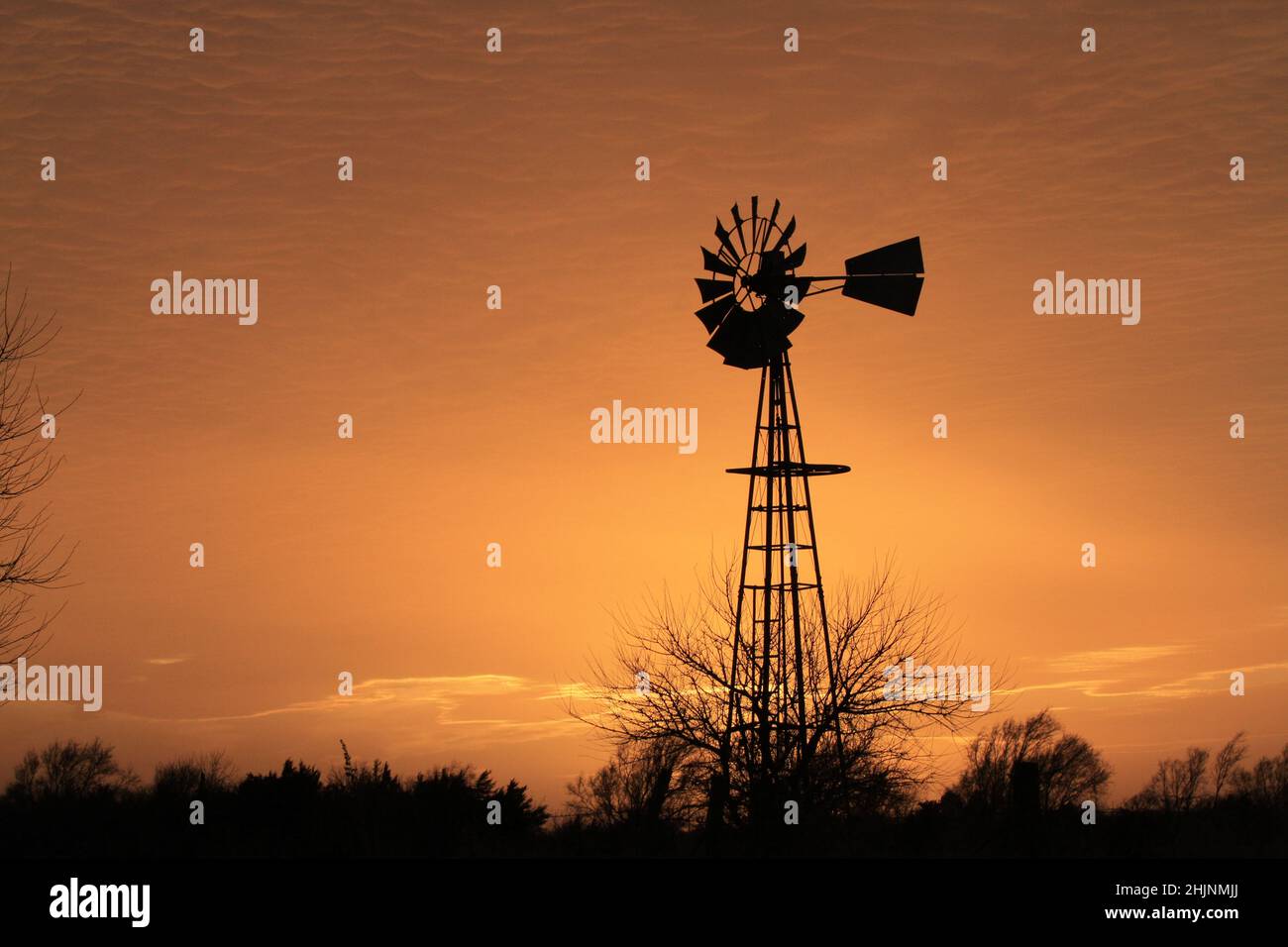 Ein farbenfroher Sonnenuntergang in Kansas mit goldenem Himmel und Windmühle auf einer Weide auf dem Land Stockfoto