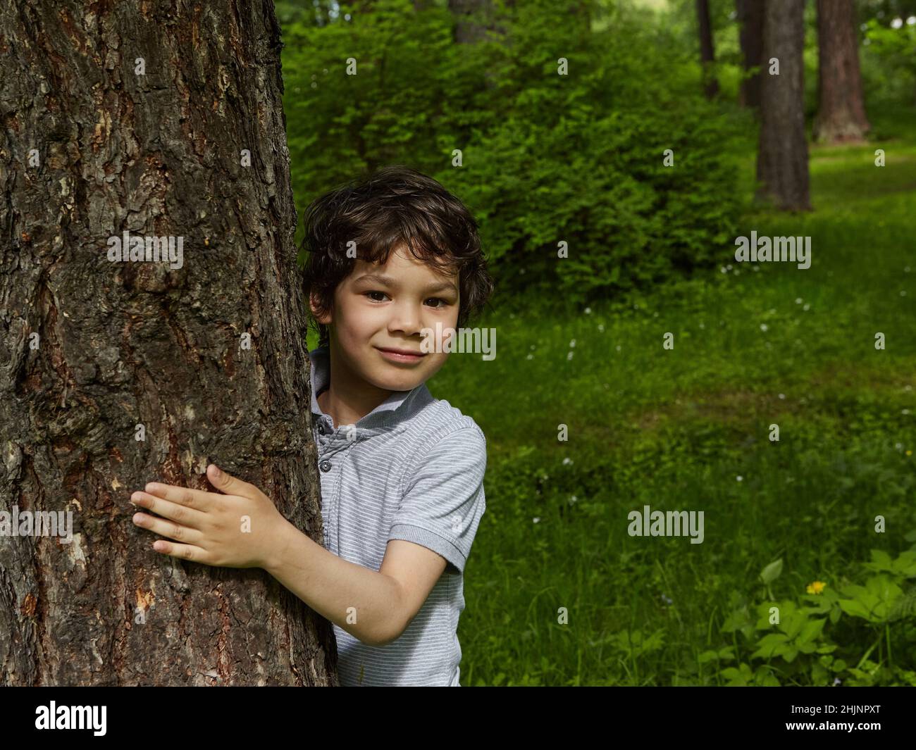 Lächelnder Junge umarmt Baum in einem Wald. . Nahaufnahme eines sorglosen Teenagers. Stockfoto