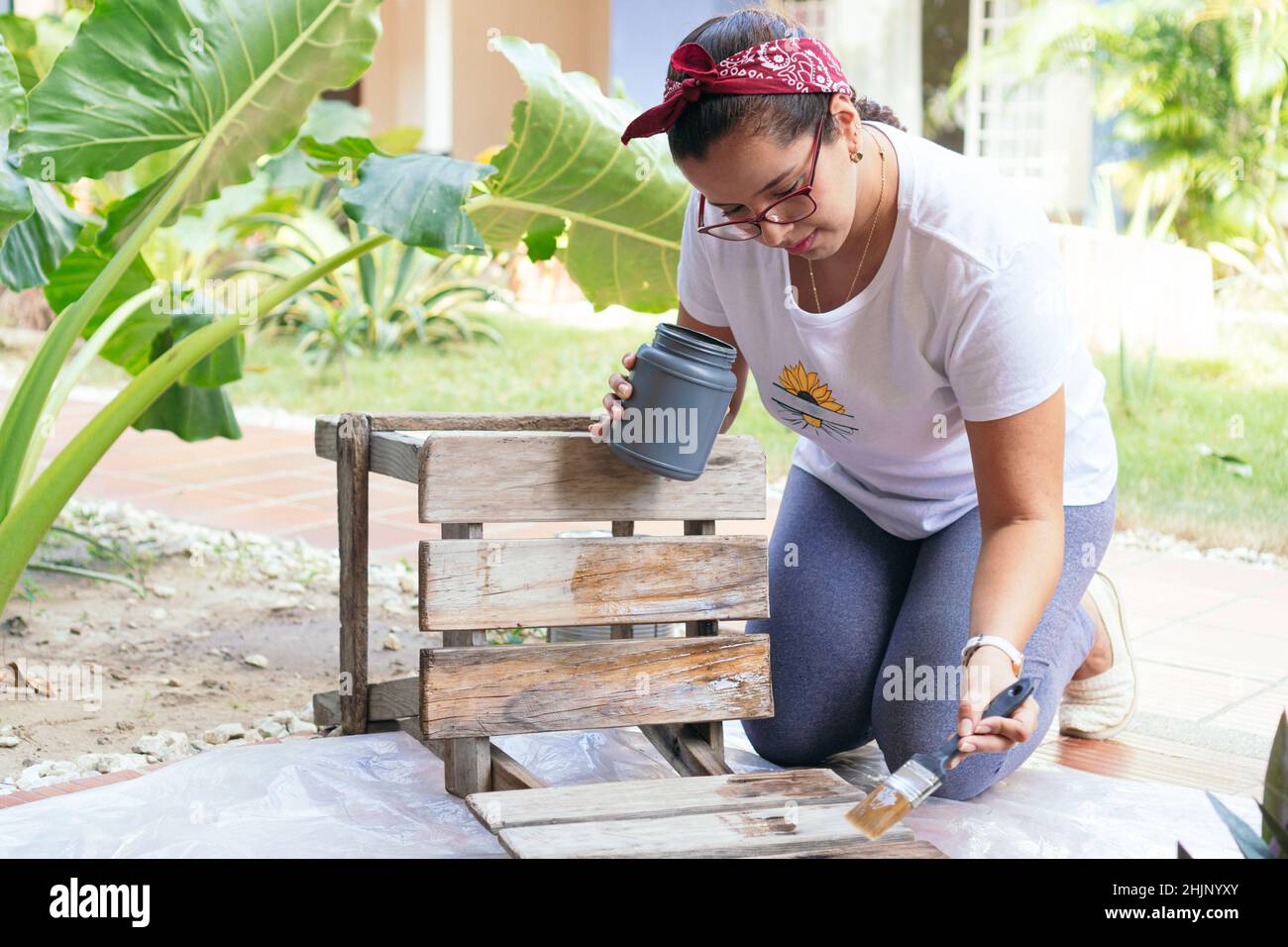 Frau malt Stuhl zu Hause. Eine Frau kniet auf einem Holzsitz auf den Boden. Stockfoto