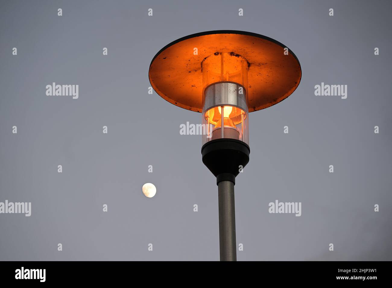 Straßenlampe mit warmem Licht und einem Kupferdach gegen einen grauen Himmel mit einem kleinen, zunehmenden Mond, Kopierraum Stockfoto