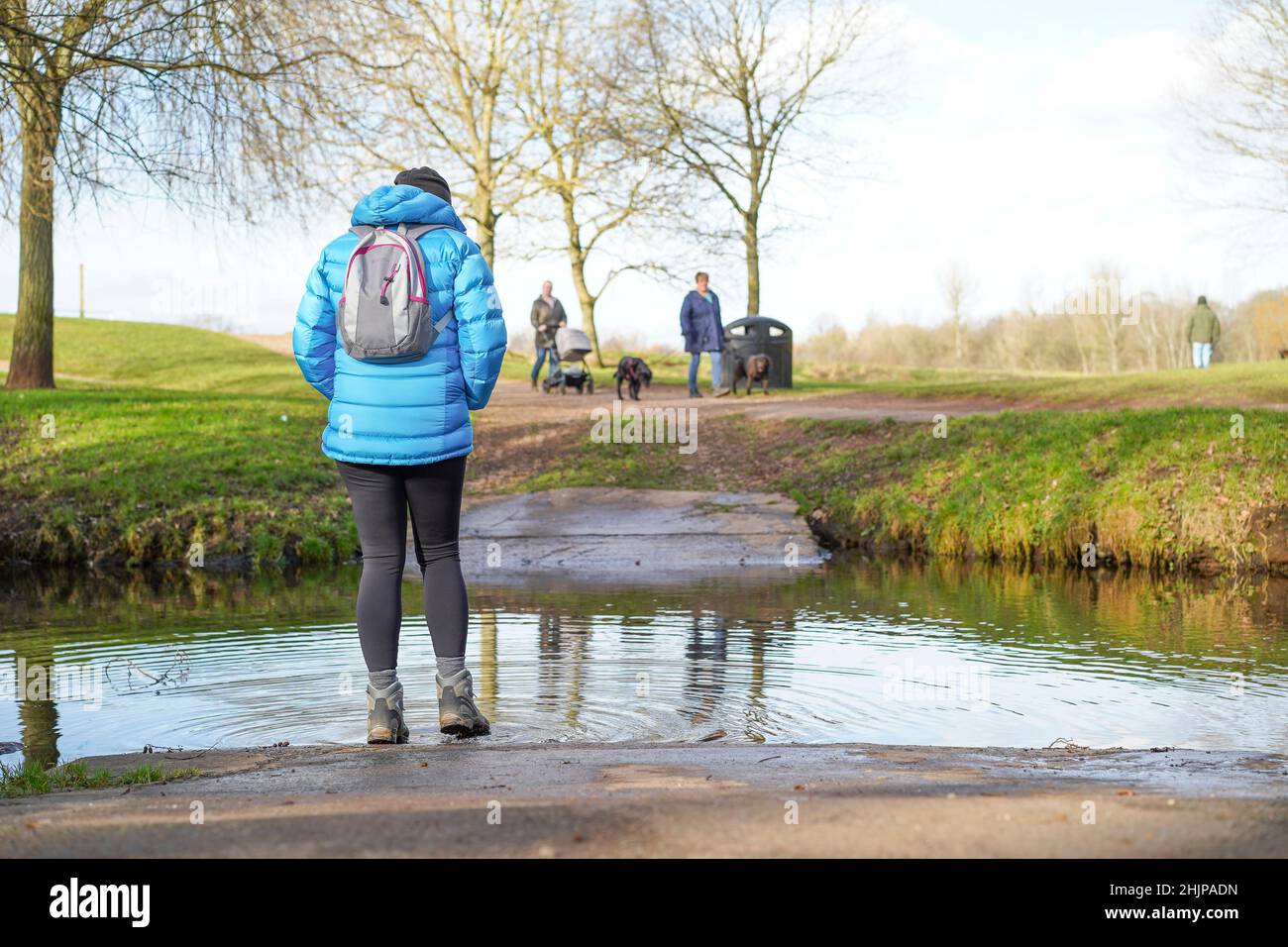 Rückansicht einer isolierten Frau, die ihre schlammigen Stiefel im Fluss eines Parks in Großbritannien putzte. Stockfoto