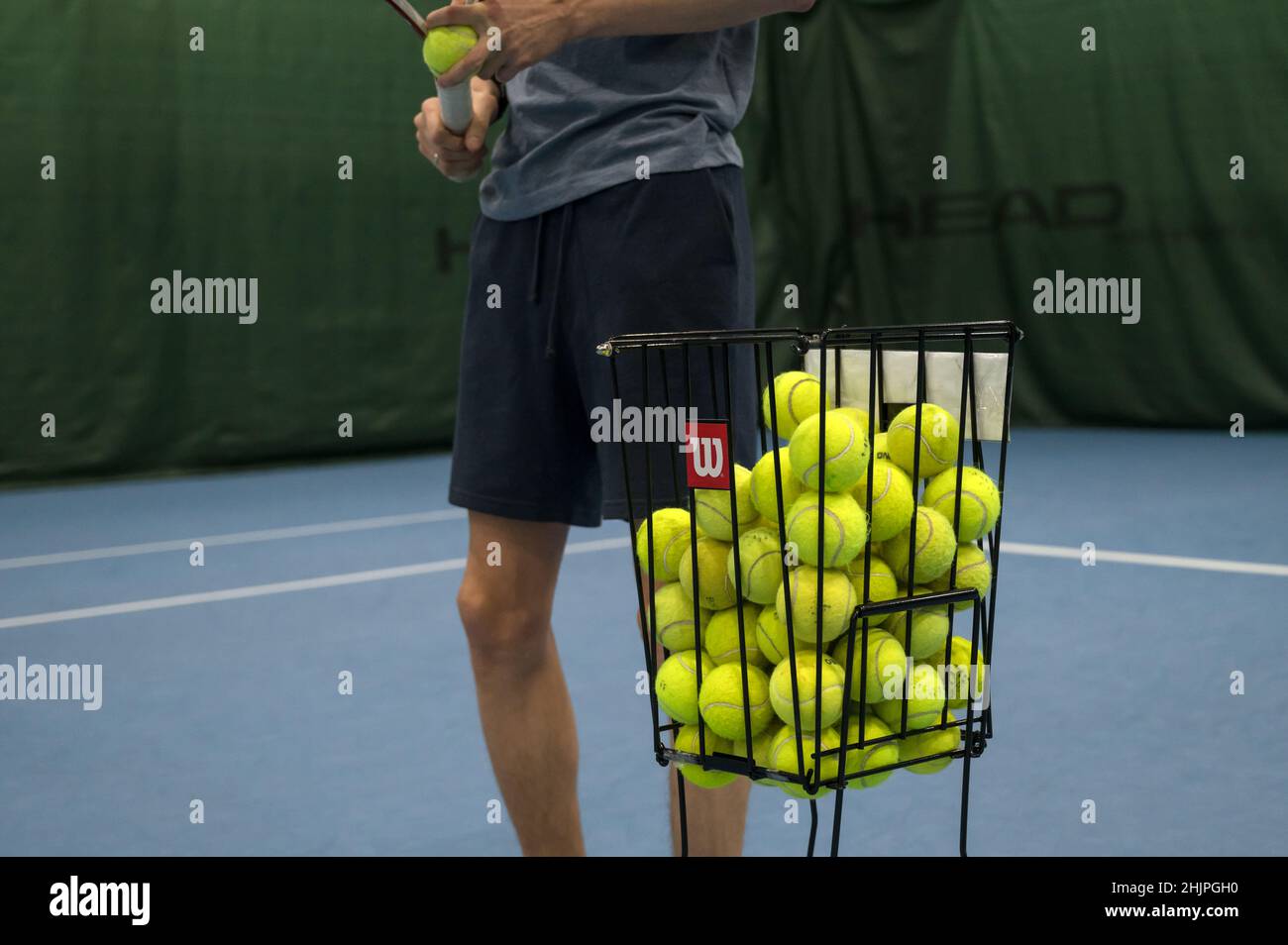 Korb mit Tennisbällen. Training auf dem blauen Hartplatz. Stockfoto
