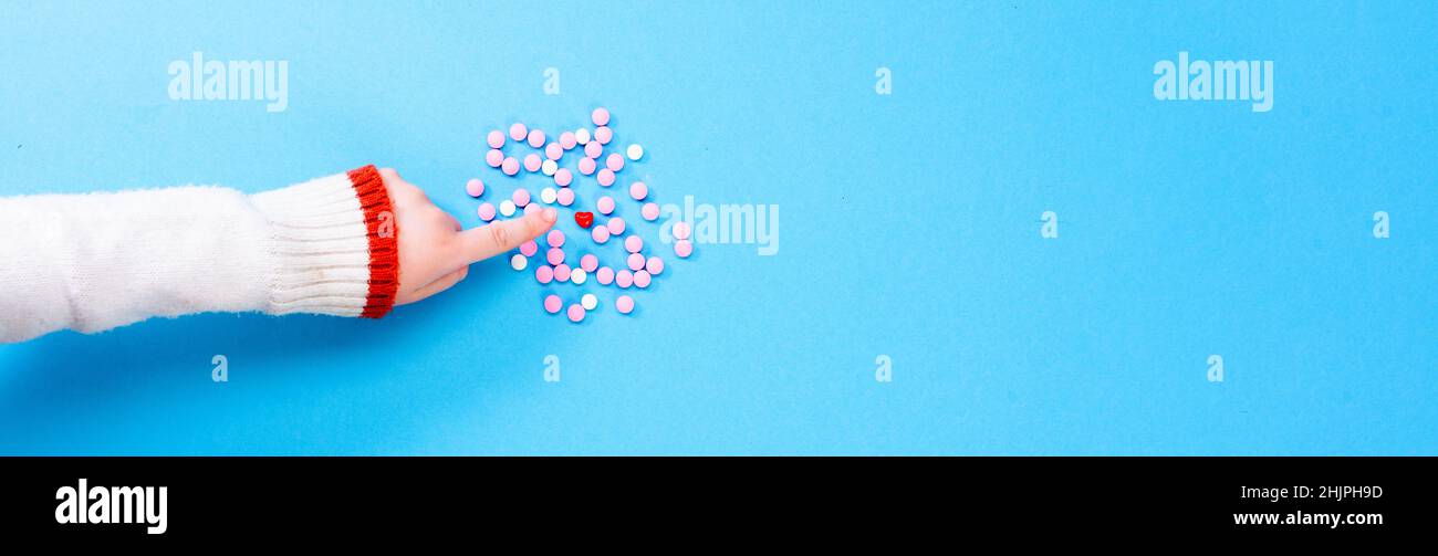 Rosa Pillen auf blauem Hintergrund mit einem Herz in der Mitte. Herzgesundheitskonzept. Die Kinderhand zeigt ein Herz zwischen rosa Pillen. Stockfoto