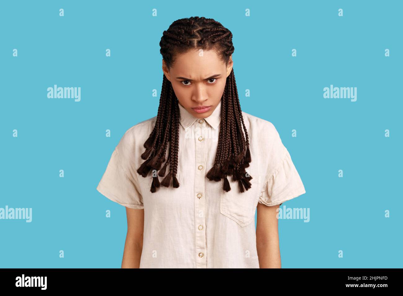 Porträt einer aggressiven Frau mit schwarzen Dreadlocks, mit Irritationen schielt Gesicht, ärgerlich über etwas, trägt weißes Hemd. Innenaufnahme des Studios isoliert auf blauem Hintergrund. Stockfoto
