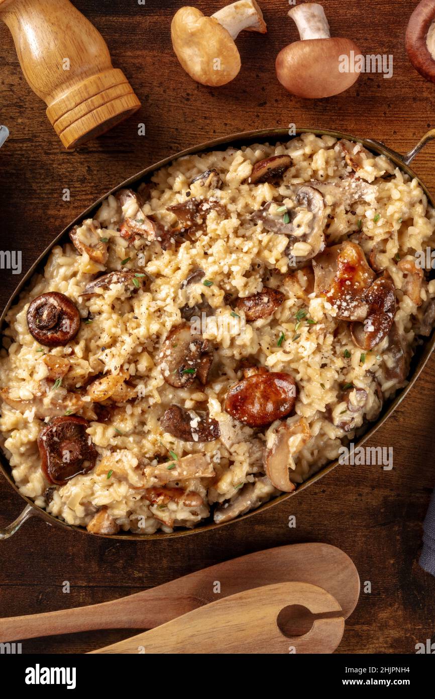 Risotto ai funghi, rustikaler Pilzreis, mit Zutaten, von oben auf dunklem Holzgrund geschossen Stockfoto