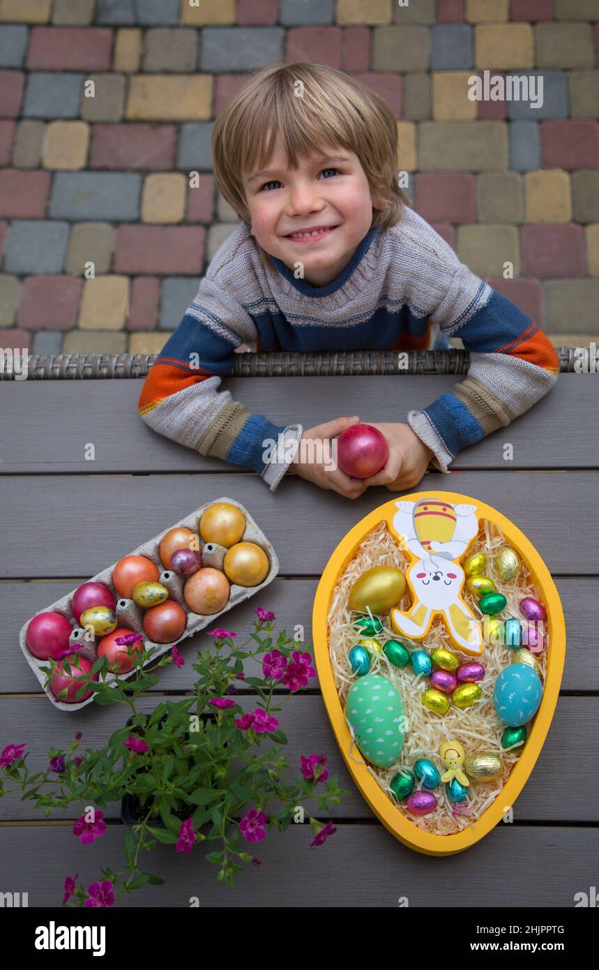 Happy Preschool Junge steht neben dem Tisch mit Ostern Dekor. Bunte Huhn, Wachtel und Schokoladeneier. Familientraditionen, freudige Kindheit. Frohes Ea Stockfoto