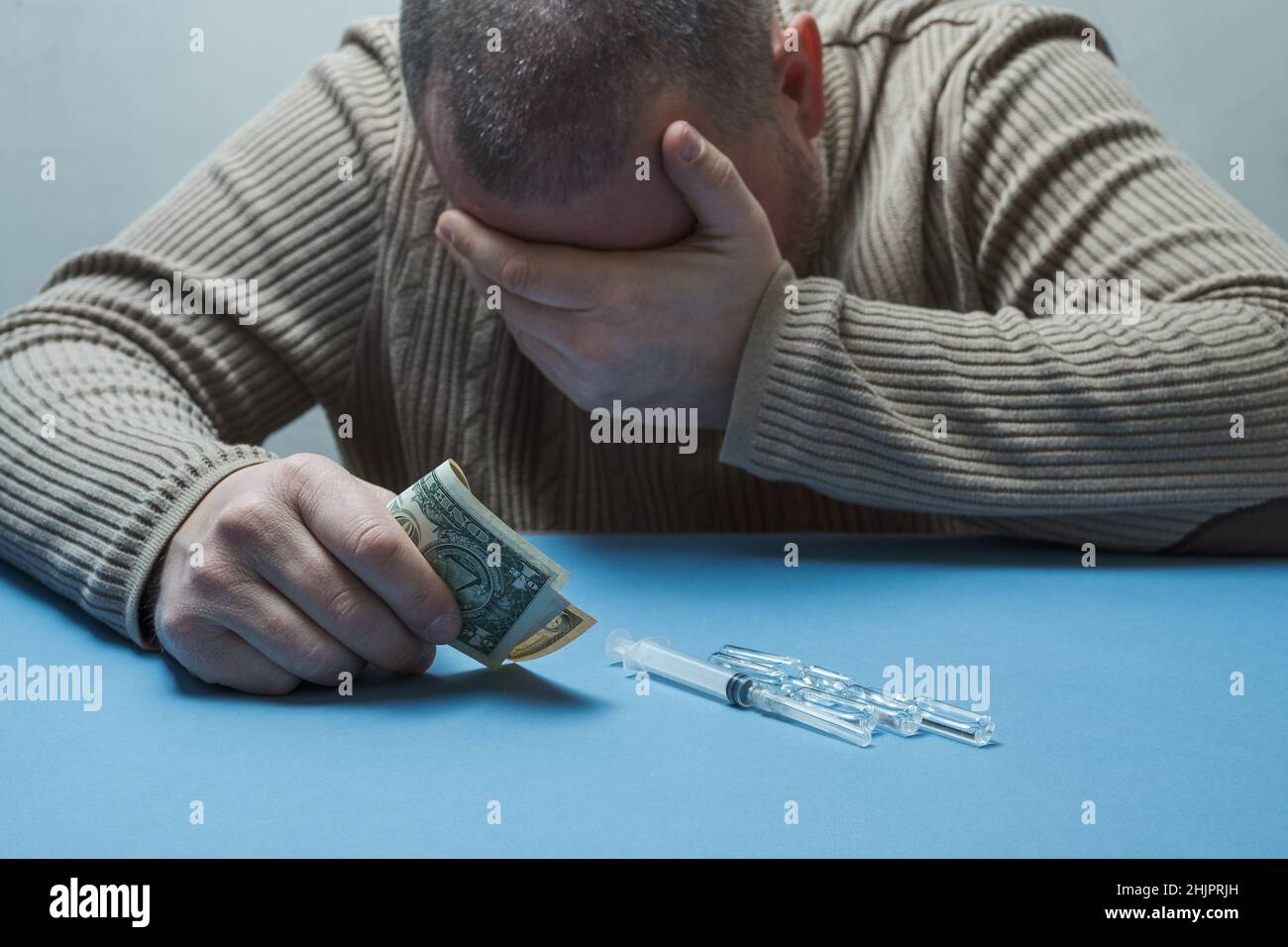 Der Mann versteckt sein Gesicht mit einer Hand, hält Geld in der anderen, medizinische Präparate liegen vor ihm auf dem Tisch. Stockfoto