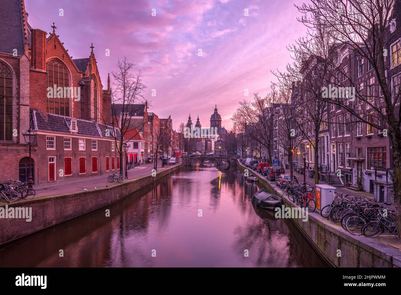 St. Nicolas Kirche und Brücke mit Blick auf einen Amsterdamer Kanal bei Sonnenaufgang mit Kanalbooten und Fahrrädern Amsterdam Holland Stockfoto