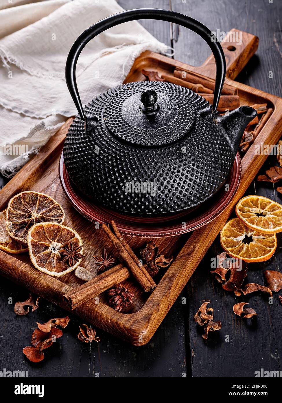 Schwarze Teekannen aus Gusseisen. Zimtstangen, Sternanisgesteine, trockene Orangenscheiben und getrockneter Ingwer auf einem Schneidebrett. Stillleben. Speicherplatz kopieren. Vertikale Aufnahme Stockfoto