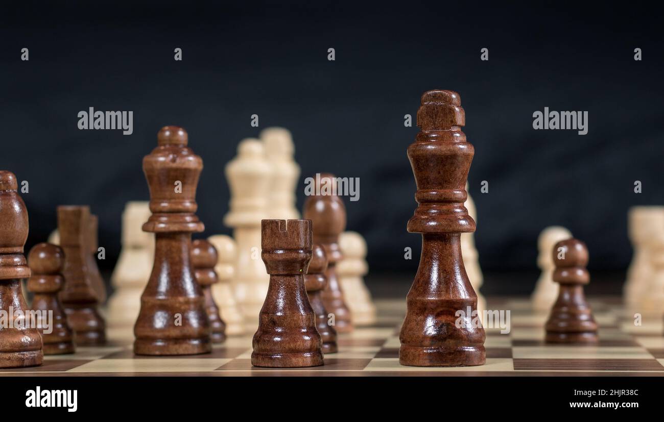 Schachbrett mit Schachspiel, das vor dunklem Hintergrund Black's Queen, Rook und King im Fokus gespielt wird Stockfoto