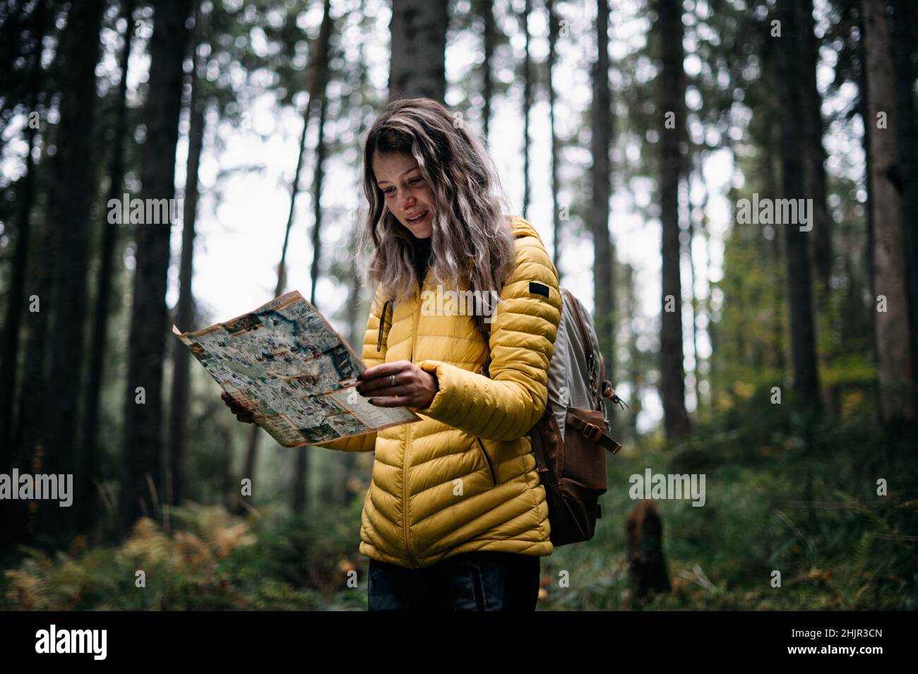 Glückliches Mädchen mit gelber Jacke beim Lesen der Karte im Wald Stockfoto