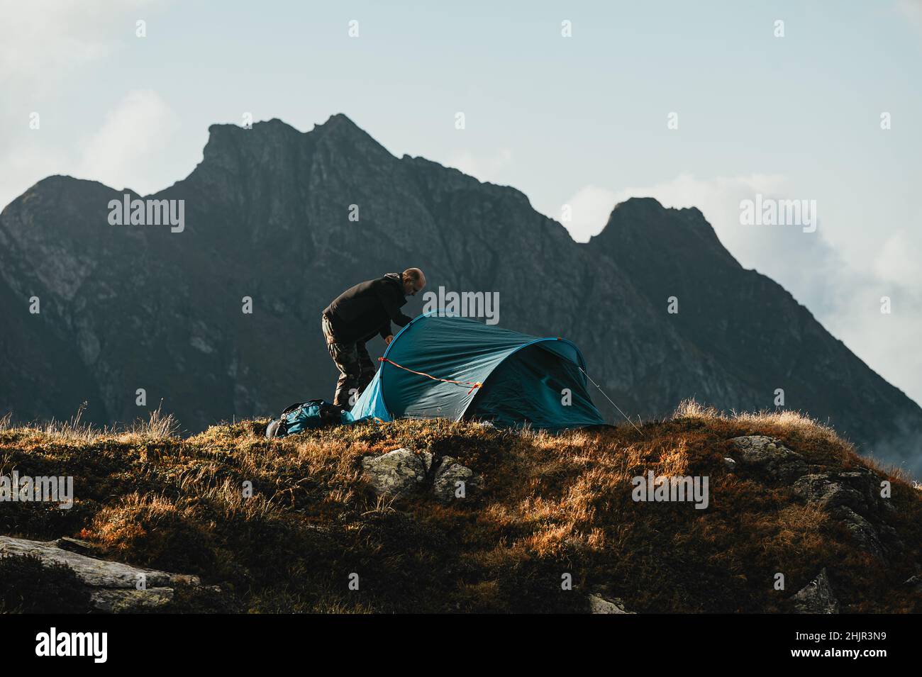 Mann, der auf dem Campingplatz Zelt aufsetzt, mit Bergen im Hintergrund Stockfoto