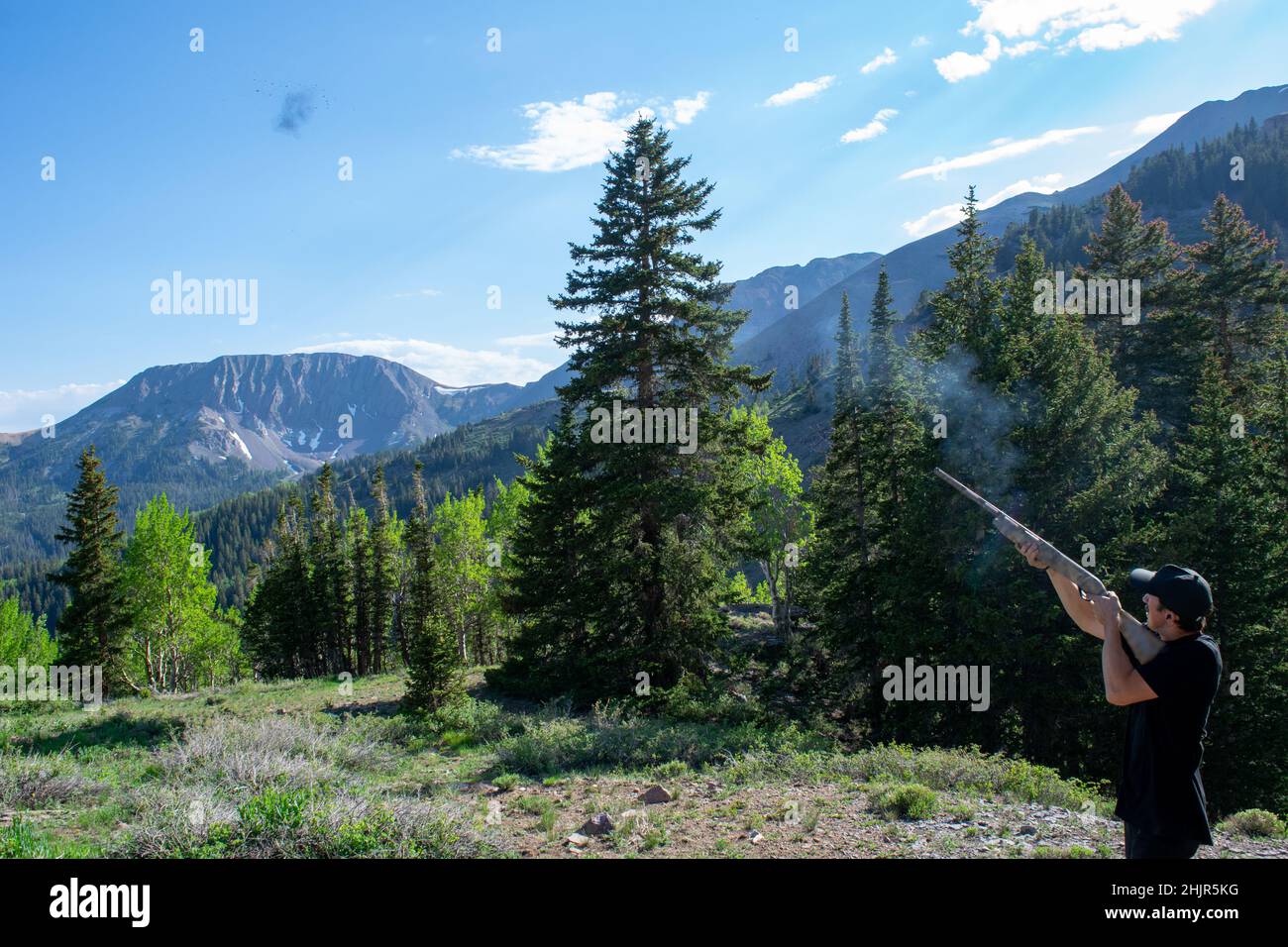 25-30-jähriger kaukasischer Mann schießt auf den Bergen Schrotflinte Stockfoto