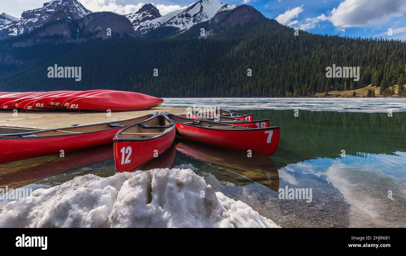 Rote Kajaks auf dem mit einer dünnen Eisschicht überzogenen Lake Louise Stockfoto