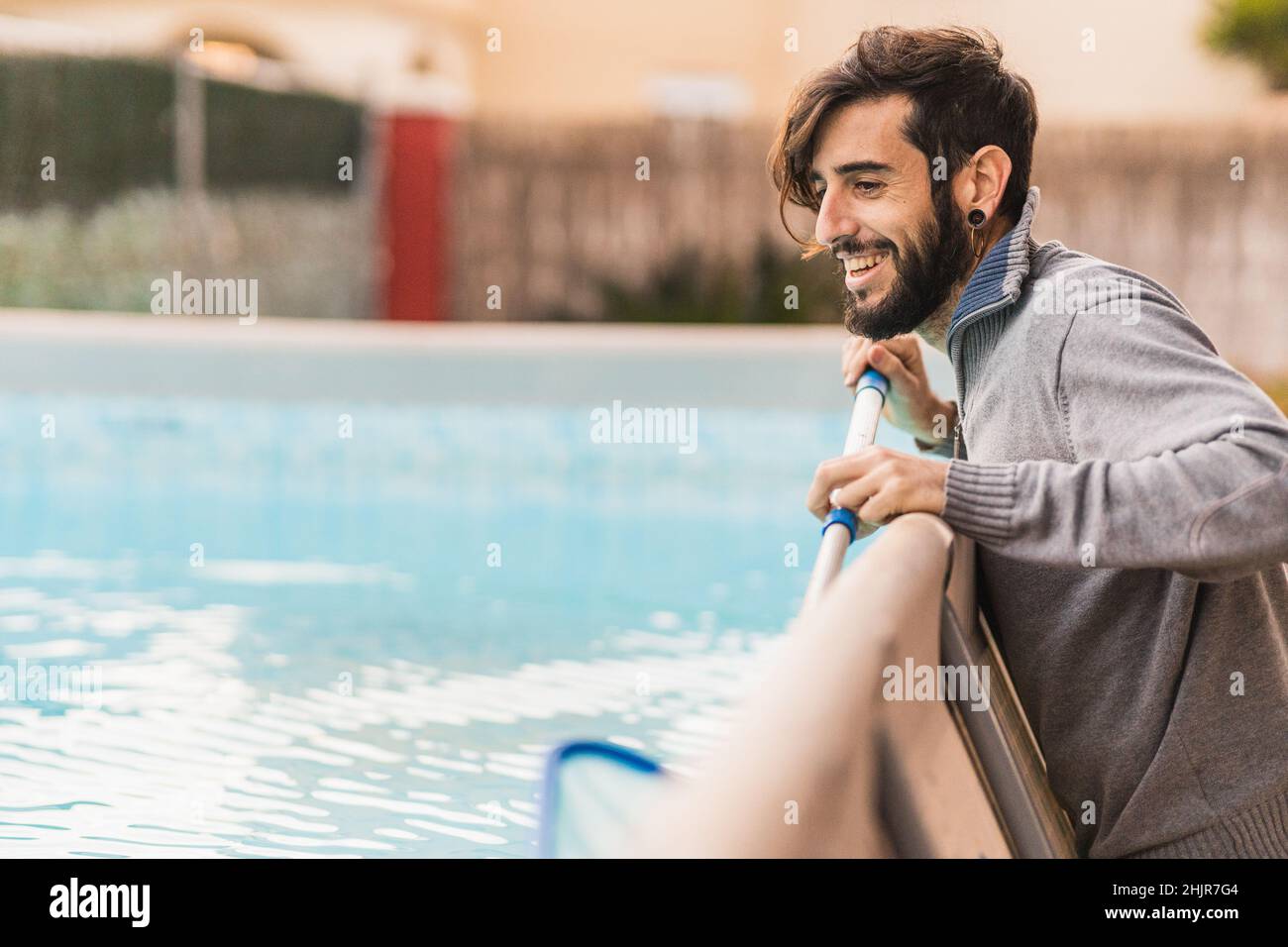 Lächelnder Hipster-Mann, der zu Hause Poolpflege macht Stockfoto