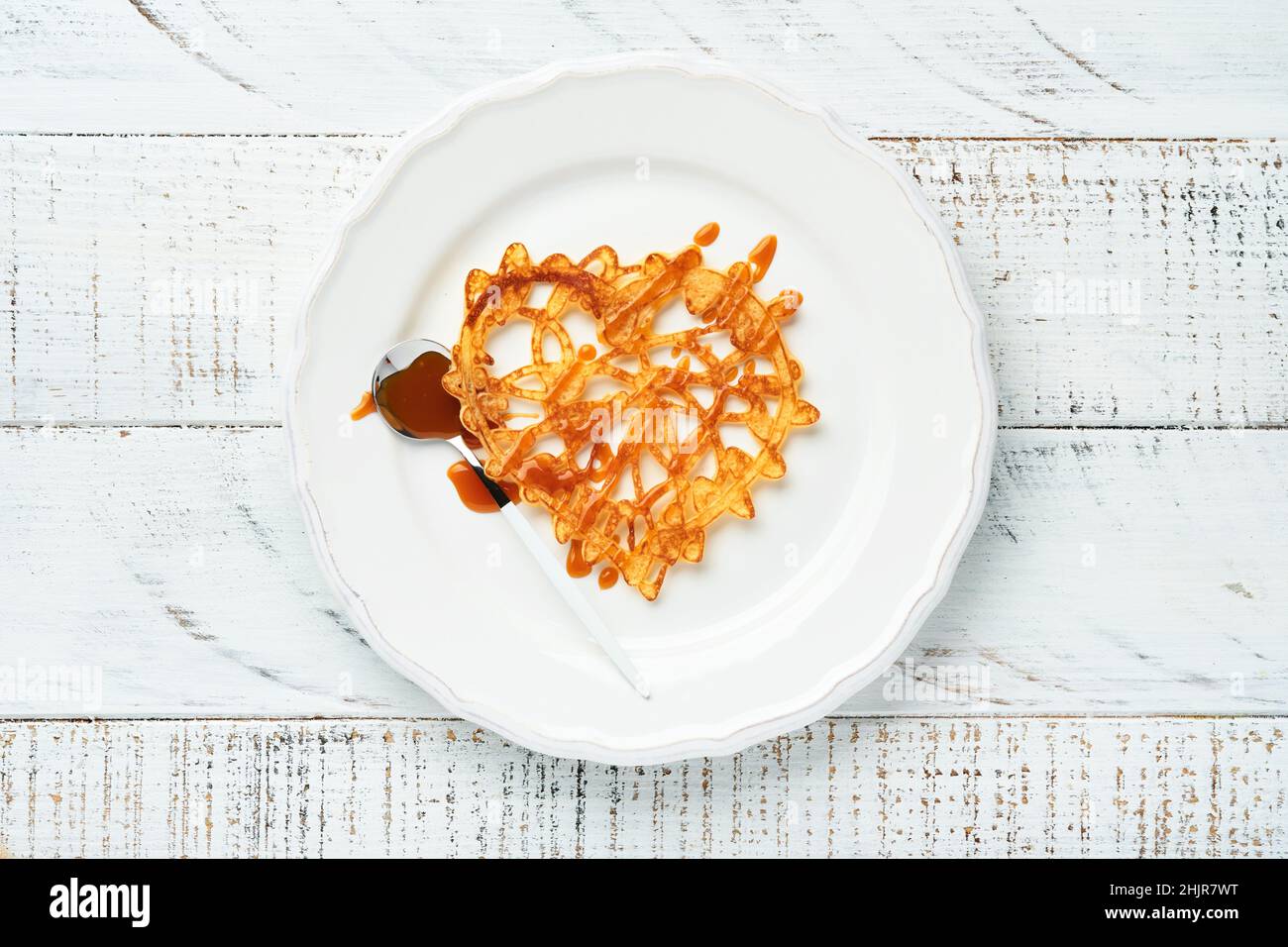 Herzförmige Spitzenpfannkuchen oder Crepes mit Karamell auf weißem Teller auf altem rustikalem Hintergrund. Tischeinstellung für Ihren Lieblings Valentinstag br Stockfoto