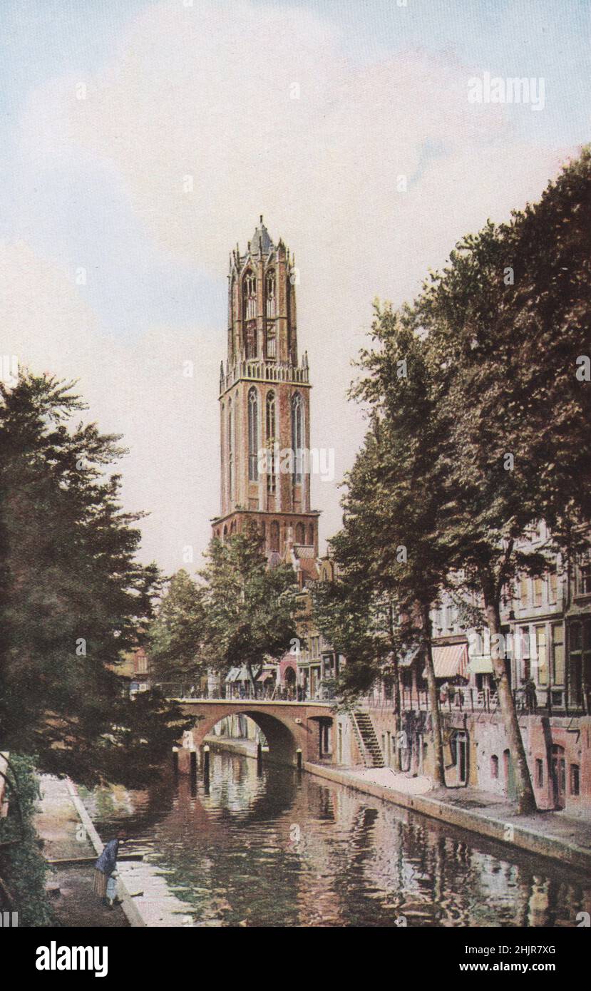 Der 338 Meter hohe Kathedralenturm aus dem 14. Jahrhundert ragt stolz über die altmodischen Wohnungen und Wasserstraßen von Utrecht. Niederlande. Niederlande (1923) Stockfoto