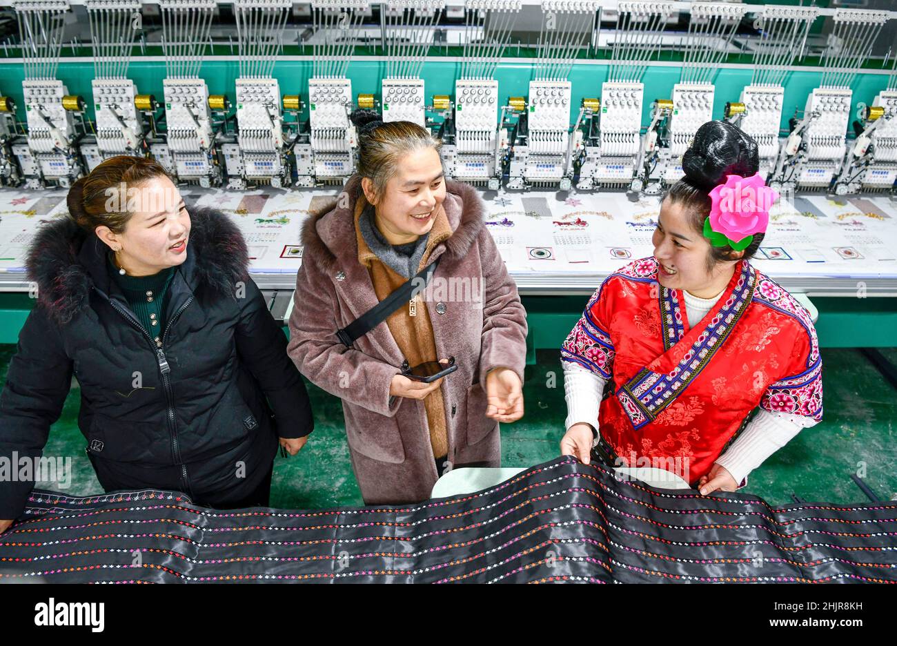 (220131) -- KAILI, 31. Januar 2022 (Xinhua) -- Yang Mei (R) stellt einem Kunden (C) in ihrer Bekleidungsfabrik in Kaili, südwestlich der Provinz Guizhou, das Tuch für ethnische Kleidung vor, 30. Januar 2022. Das Dorf Kaishao, die Heimatstadt des Stickerers Yang Mei, war aufgrund seines schlechten Bodens und der begrenzten Transportbedingungen verarmt. Viele Dorfbewohner hier entschieden sich, als Immigranten an anderen Orten zu arbeiten. Dank der lokalen Politik zur Armutsbekämpfung erhielt Yang Mei's Familie im Jahr 2016 die Chance, in ihr neues Zuhause an einem Umzugsort in Kaili zu ziehen. Mit Hilfe von Skill-Trainings und support Stockfoto