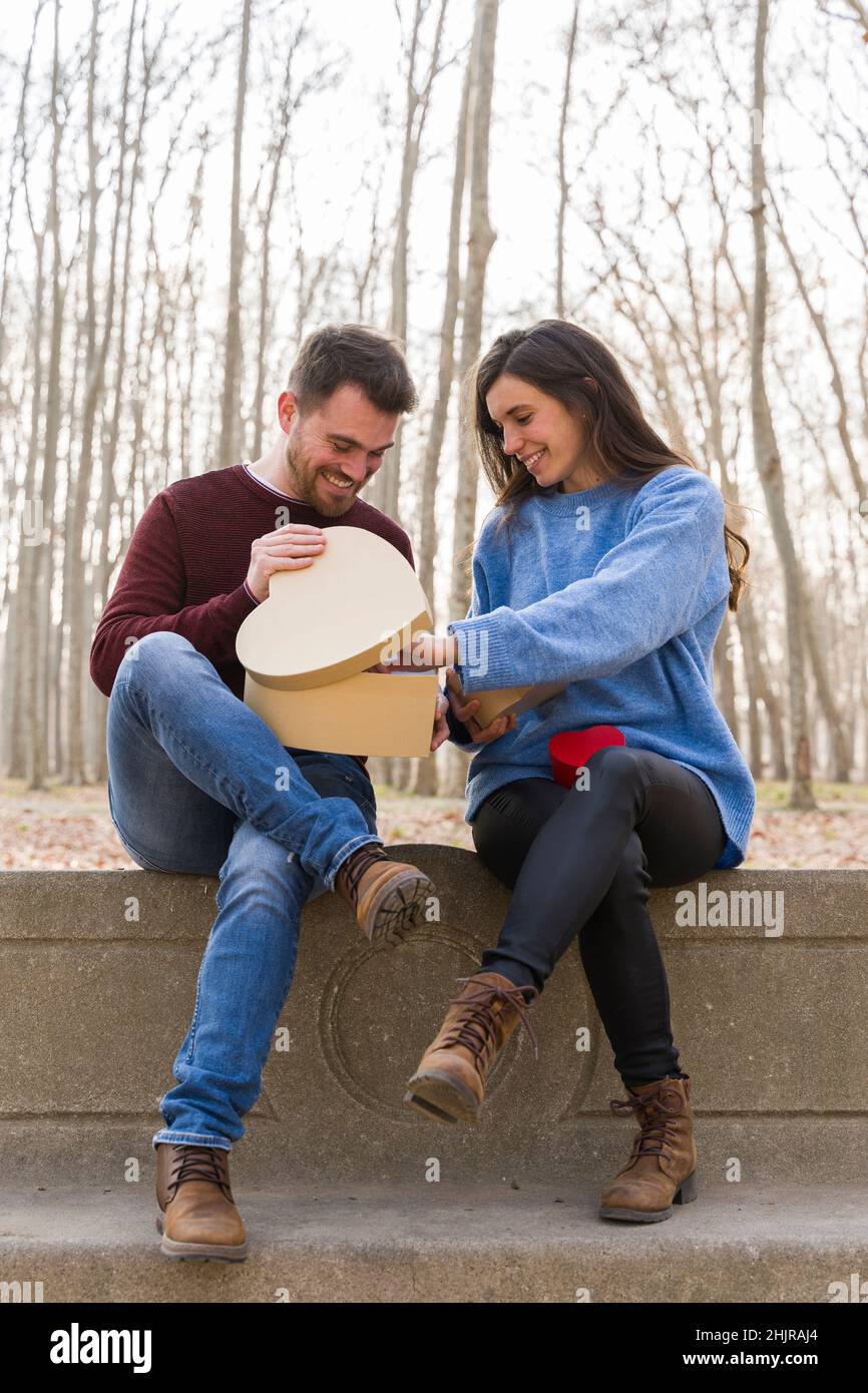 Junges Paar, das den valentinstag feiert und sich gegenseitig ein Geschenk in einem Park schenkt Stockfoto