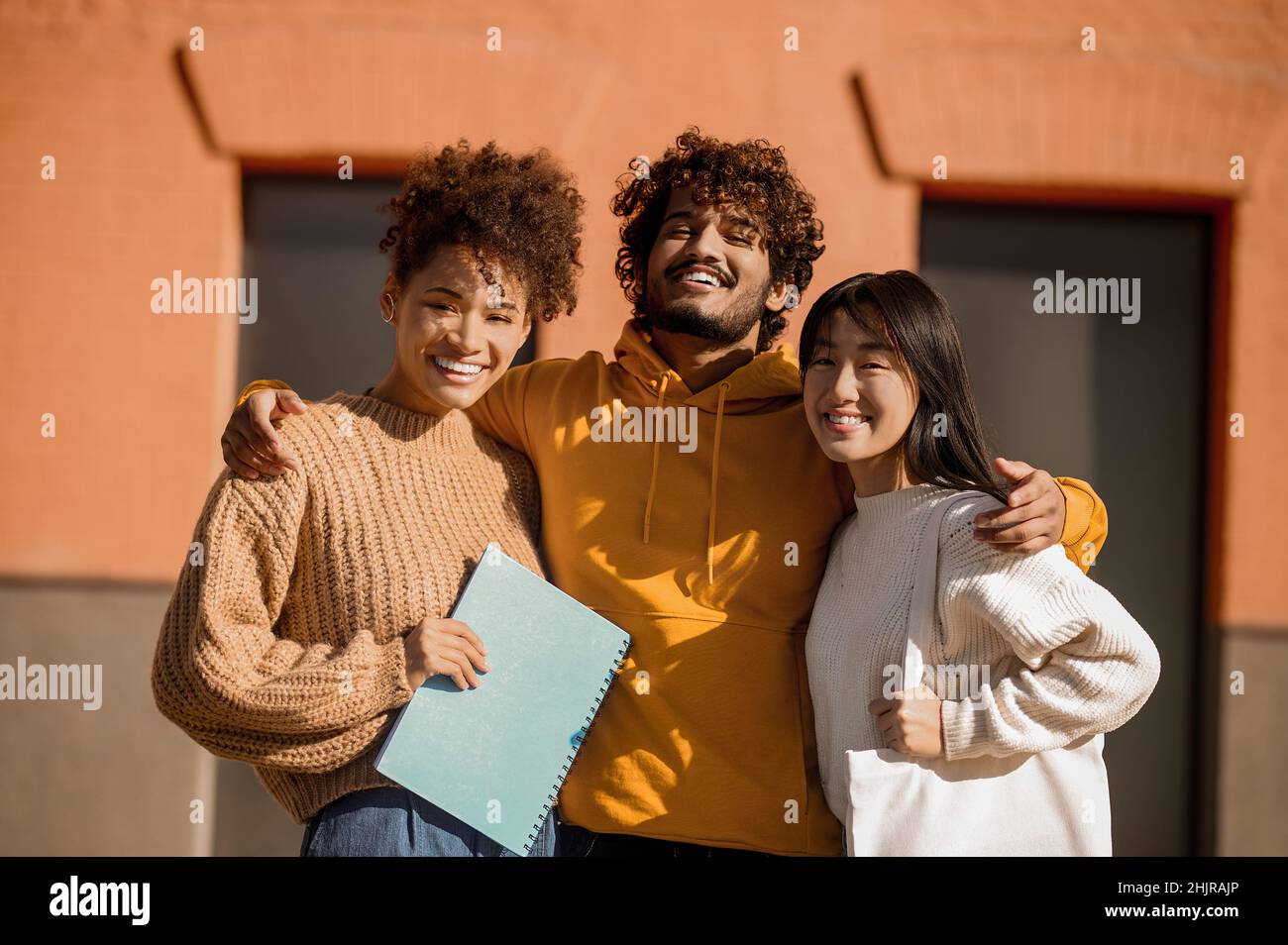 Guy umarmt zwei Mädchen und schaut auf die Kamera Stockfoto