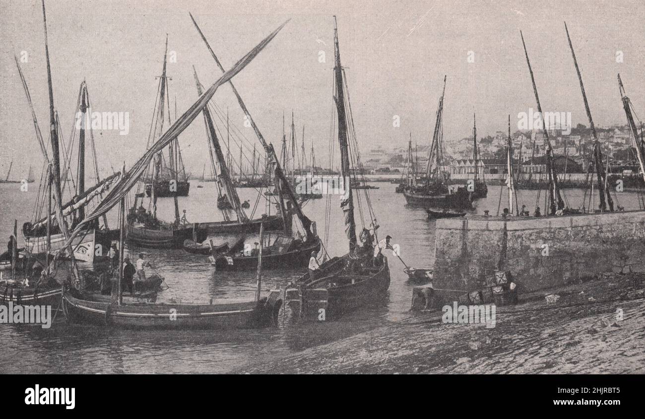 Fischerboote im Hafen, unterstützt von der Stadt, die die Hügel über dem Tejo aufsteigt. Portugal. Lissabon (1923) Stockfoto