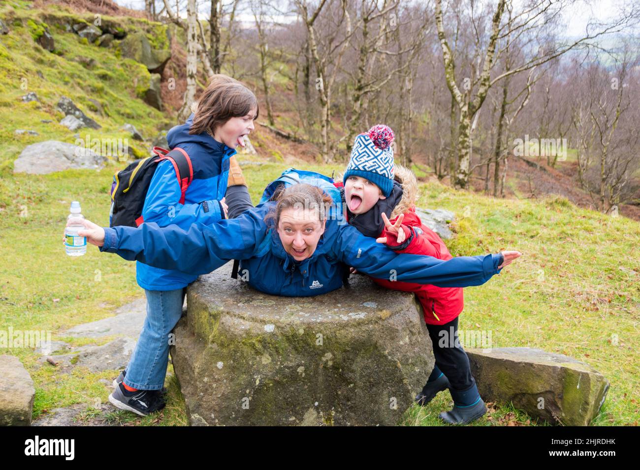 Eine Frau und zwei Jungen posieren für ein Foto, das auf einem Mühlstein ‘fliegend’ liegt, während die Kinder mit ihren Zungen Gesichter herausziehen, Bolehill Quarry, Peak Distri Stockfoto