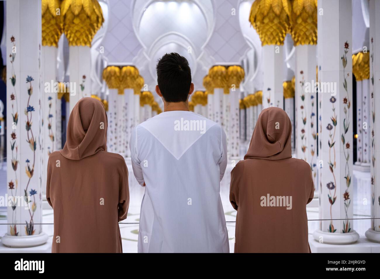 Ein Mann und zwei Frauen, die in traditioneller arabischer Kleidung mit den Armen in der Kolonnade der Großen Moschee stehen, von hinten geschossen Stockfoto